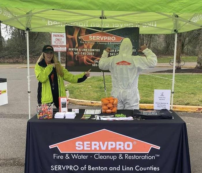 SERVPRO Green Pop-Up Tent and table with female Representative pointing to a gentleman in a Hazmat Suit